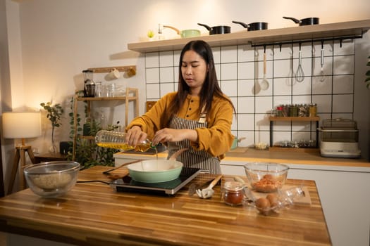 Young woman pouring cooking oil into a frying pan, ready to start the meal preparation.