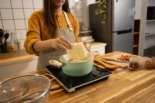 Close up shot of woman putting dried instant noodles into a boiling pot.