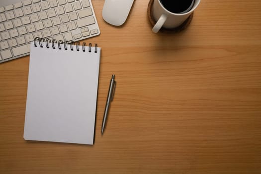 Simple workspace with a spiral notebook and a cup of coffee on wood desk.