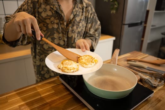 Man preparing breakfast in modern kitchen, serving freshly cooked eggs on a plate.