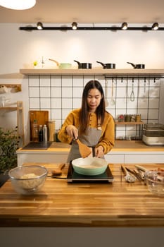 Happy young asian woman cooking in a stylish modern kitchen. Home cooking concept.