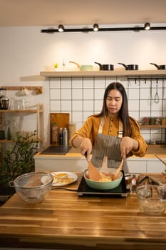 Happy young asian woman cooking in a stylish modern kitchen. Home cooking concept.