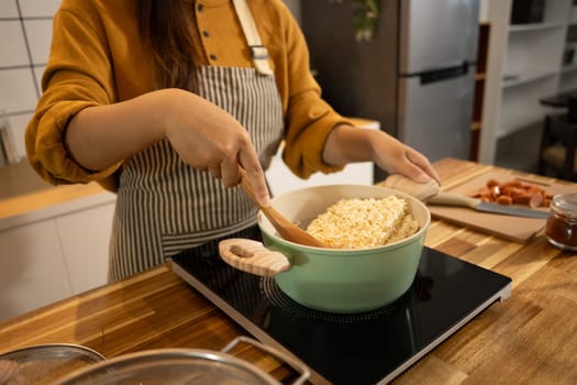 Close up shot of woman placing a block of instant noodles into a green pot.