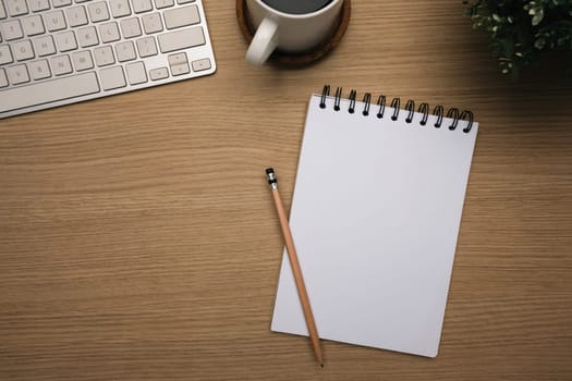 Top view of wooden desk with blank spiral notebook, keyboard and a cup coffee.
