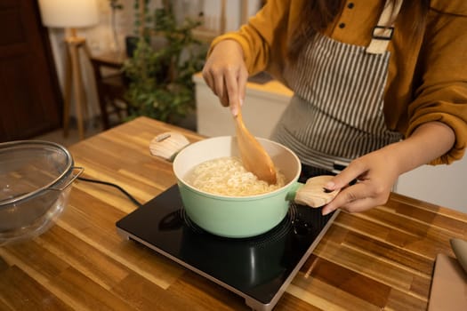 Close up shot of woman stiring instant noodles in a boiling pot.