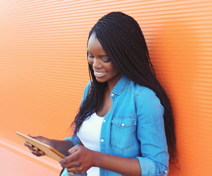 Modern happy black American young woman using digital tablet computer, black girl looking at device on city street