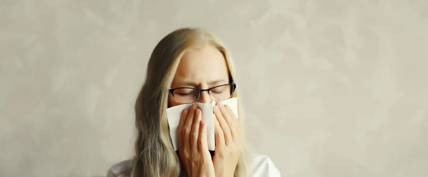 Sick exhausted mature woman sneezing blow nose using tissue, unhealthy suffering girl feels unwell at home