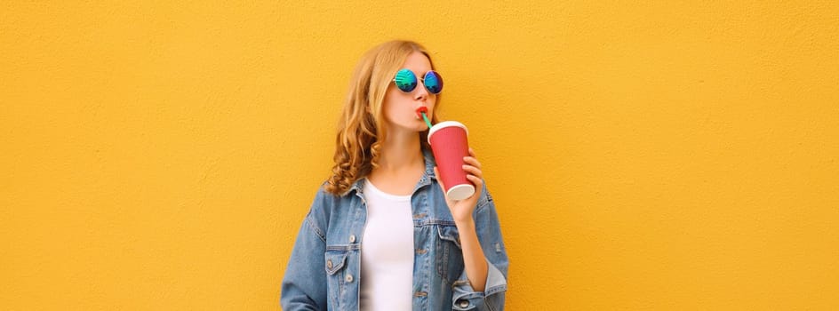 Summer vacation, modern young woman with cup of coffee, stylish girl drinking fresh juice posing in casual denim jacket on vivid yellow wall background