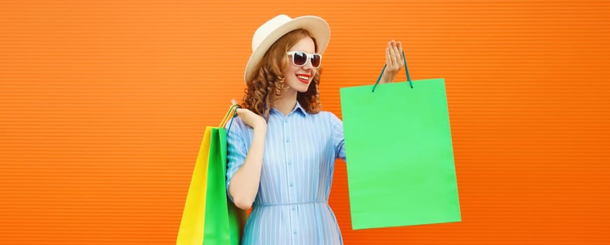 Fashion, purchase. Stylish beautiful happy young woman posing with colorful shopping bags, girl in summer hat standing on bright orange background