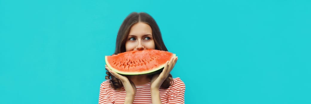 Summer portrait of happy young woman eating fresh slice of watermelon on blue studio background