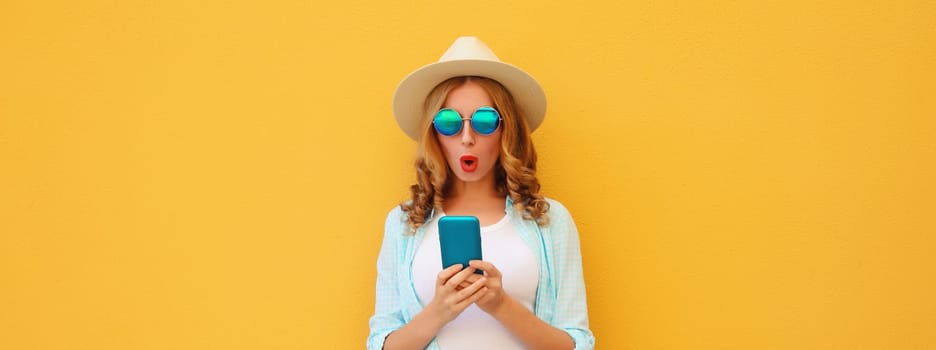 Summer vacation, surprised amazed traveler young woman with phone, shocked tourist girl looking at smartphone in straw hat on yellow studio background