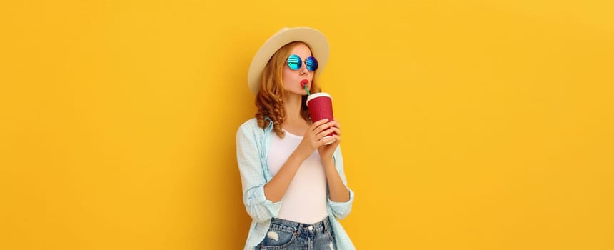 Summer vacation, beautiful modern young woman with cup of coffee, stylish girl drinking fresh juice in tourist straw hat on yellow background
