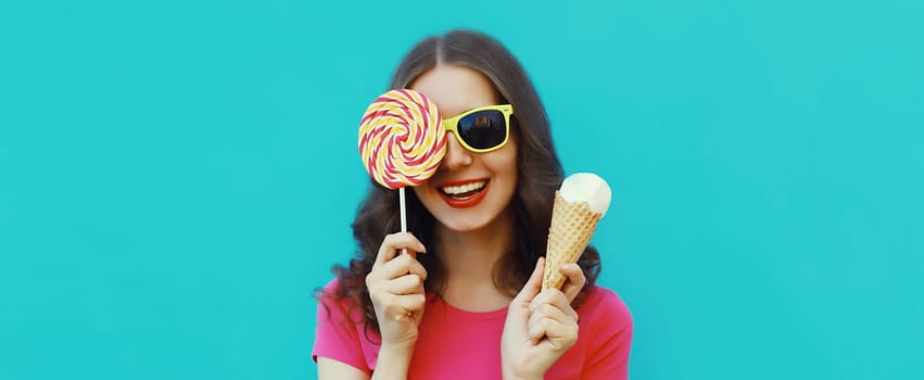 Summer portrait of happy laughing young woman holding ice cream cone and lollipop blowing a kiss on blue background