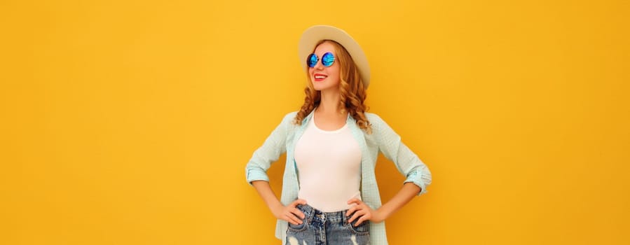 Beautiful happy young woman looks away in summer tourist straw hat, shirt and shorts posing on bright orange background