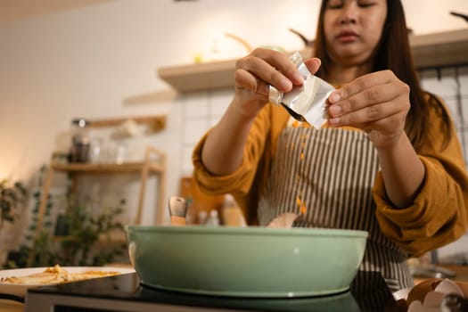 Shot of woman adding powdered seasoning to a pot of instant noodles and sausages.