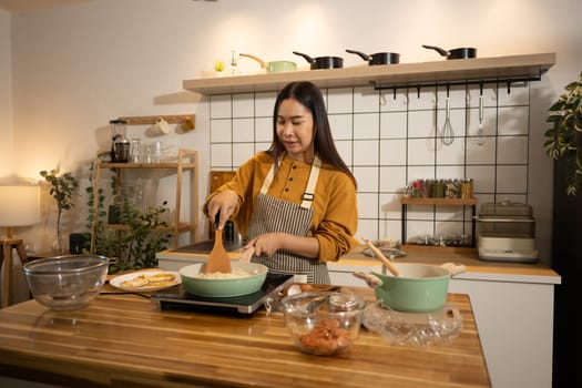 Smiling woman in apron stirring food in frying pan on an induction stove.