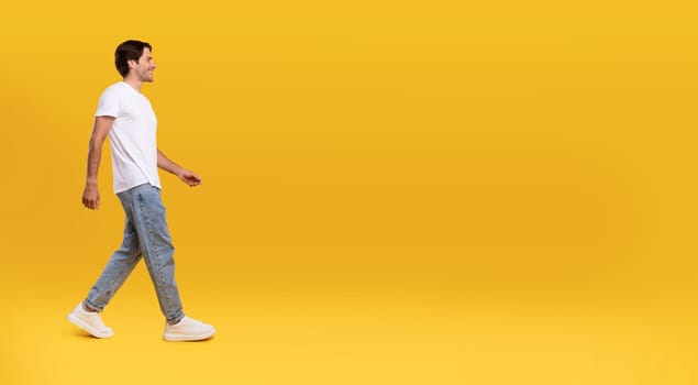 Full length body size profile side view of happy excited bearded guy in casual white t-shirt and jeans walking looking aside at free empty space isolated over orange color background, panoramic banner