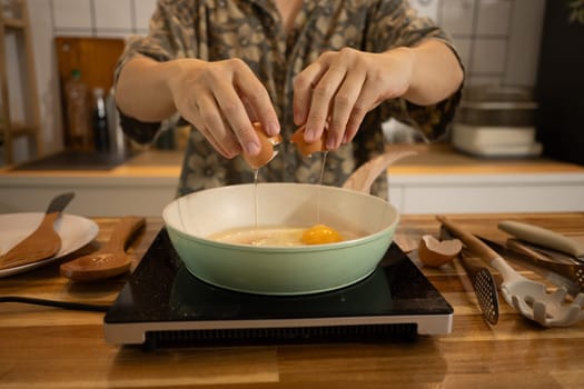 Close up shot of man cracking an egg into a frying pan, ready to prepare delicious meal.