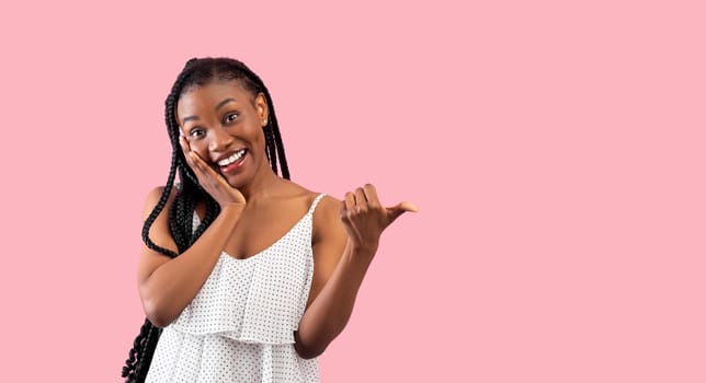Summer sale. Emotional black lady pointing at blank space over pink studio background, banner design. Pretty African American woman in trendy clothes having special offer, advertising your product