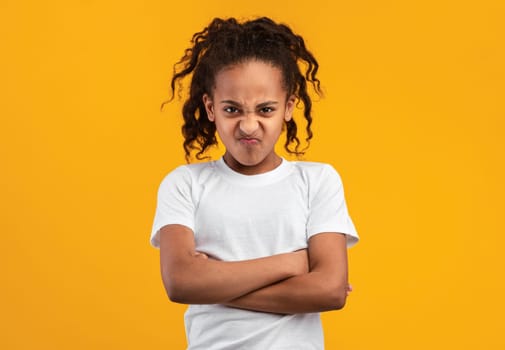 People Emotions, Teen Maximalism Concept. Portrait of offended young black girl posing with folded arms, standing isolated on yellow studio wall. Angry lady holding hands crossed, looking at camera