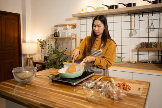 Young Asian woman preparing meal on an Induction stove in a kitchen.