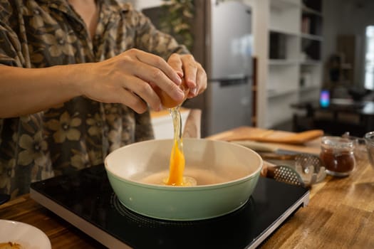 Close up shot of man cracking an egg into a frying pan, ready to prepare delicious meal.
