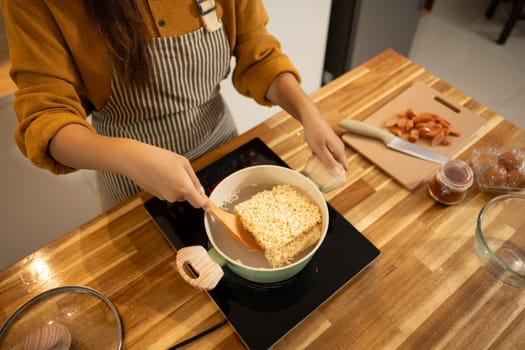 Close up shot of woman putting dried instant noodles into a boiling pot.