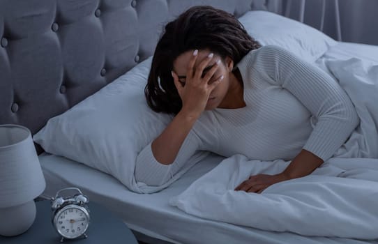 Lack Of Sleep Concept. Stressed young African American woman suffering from insomnia, lying in bed and covering face, waking up throughout the night, feeling depressed about start of the working week