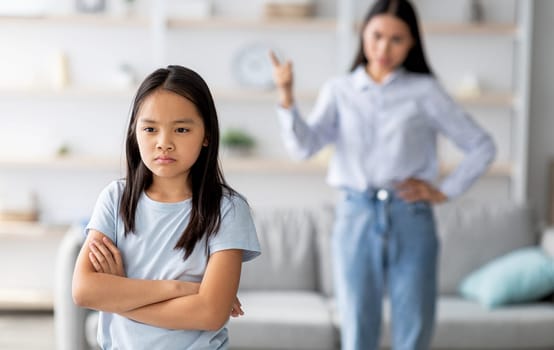 Family conflict. Mother and daughter quarreling at home, sulky child girl ignoring her mom, standing back to her with crossed arms, selective focus, copy space