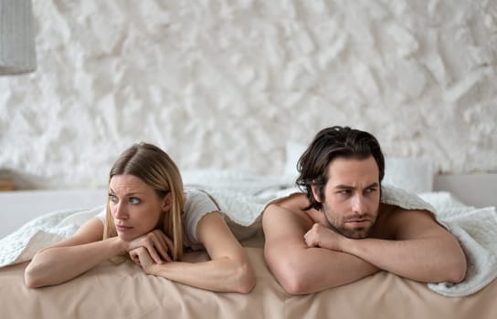 Sexual problems, relationship crisis. Stressed young couple lying in bed, overwhelmed with family difficulties, not speaking after conflict, suffering from erectile dysfunction or lack of libido