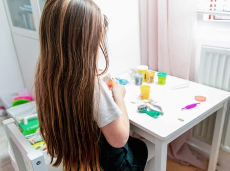 Little girl with long brown hair playing with plasticine. High quality photo