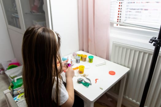 Little girl with long brown hair playing with plasticine. High quality photo