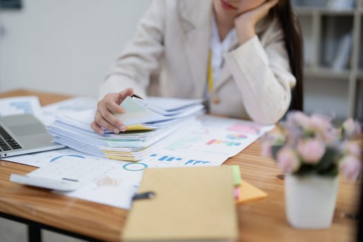 Stressed young businesswoman overwhelmed by paperwork with finance, market charts and documents in office.