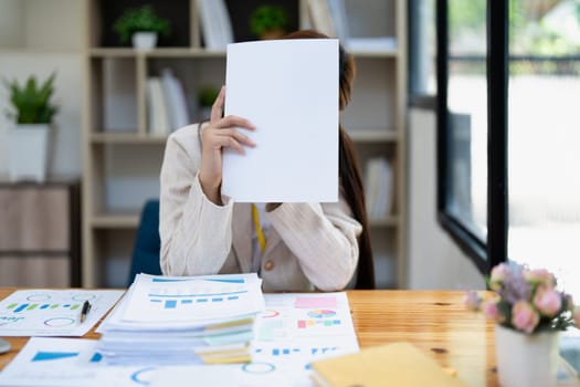 Stressed young businesswoman overwhelmed by paperwork with finance, market charts and documents in office.
