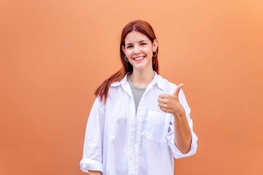 young woman giving a thumb up gesture while smiling looking at camera in a positive and friendly mood suggesting that she is happy and content, copyspace for text