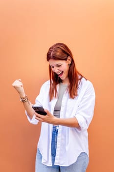 young woman holding cell phone and smiling happy while celebrating with clenched fist, concept of positivity and enjoyment of technology, copyspace for text