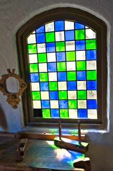 Colorful stained glass window in historical surroundings. Play of light on rustic wooden table with antique tools. Nostalgic atmosphere in vintage style