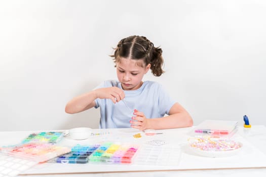 Little girl enjoys crafting colorful bracelets with vibrant clay beads set.