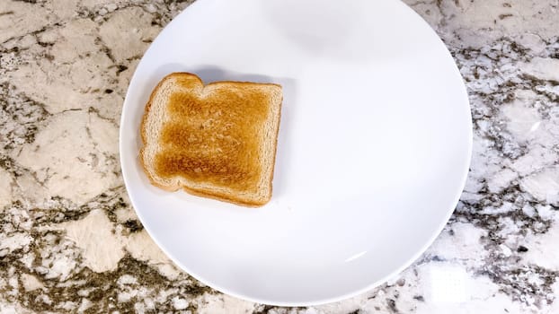 White plate holds a slice of golden-brown toast and two fried eggs, served on a textured marble countertop, offering a classic breakfast choice.
