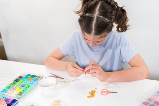 Little girl enjoys crafting colorful bracelets with vibrant clay beads set.