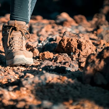 Legs in high hiking boots of coyote color with a textured sole close-up, a girl walks along a path in the mountains, rocky terrain in comfortable shoes for active pastime in a daytime.