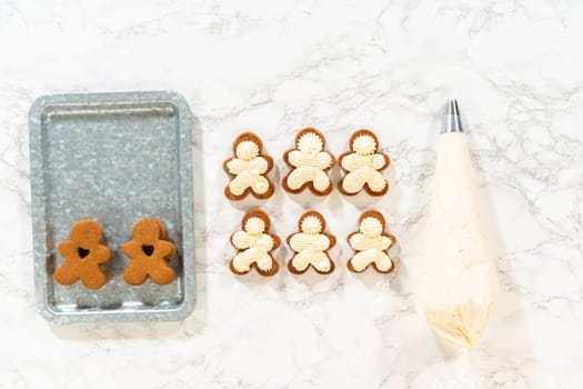 Flat lay. Gingerbread cookies await their second halves on a marble surface, each meticulously piped with buttercream to craft delightful sandwich treats. The precision of the piping adds a festive touch.