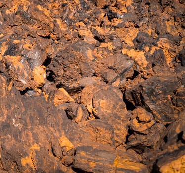 Texture of fossilized lava formation after volcano antient erruption in a rock of red shades on a volcanic terrain, black basal inside a stone close-up in the rays of a sun.
