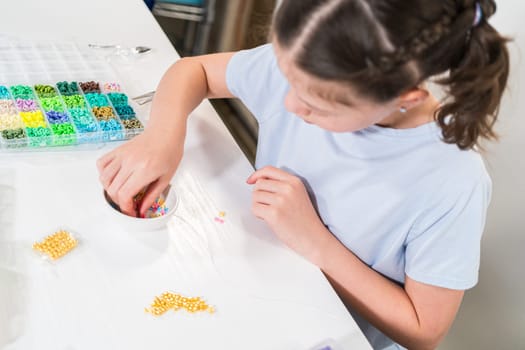 Little girl enjoys crafting colorful bracelets with vibrant clay beads set.
