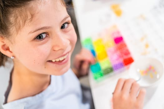 Little girl enjoys crafting colorful bracelets with vibrant clay beads set.