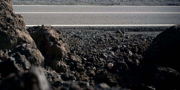 An atmospheric asphalt road among volcanic black basalt lava formations, the path is an empty scenic highway without people running through dramatic volcanic terrain with volcanoes.