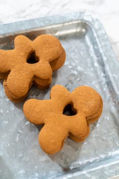 Gingerbread cookies, including a gingerbread man with a heart-shaped cutout, rest on a rustic metal tray against a marble countertop.