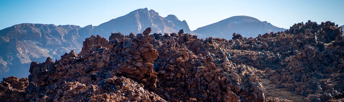 Volcanic lunar landscape in the sun with black lava formations, mountains and desert, red golden sand. Scenic dramatic view with volcanoes and rocks at sunset.