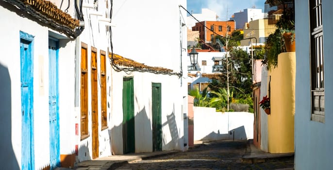 A beautiful picturesque street of the old town in the sun, houses with yellow and white walls, vintage windows and street lamps in a small village among the mountains.