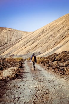 A young man leads an active lifestyle, traveling through the valley, hiking among picturesque sand mountains and volcanoes in the desert with a backpack.
